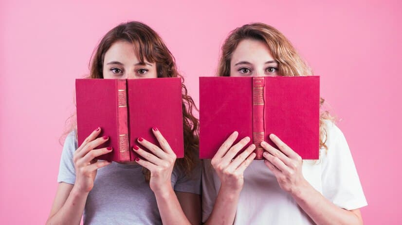 Two Girls Holding Books at Pink Background